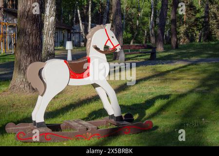 Cavallo di legno bianco nel parco su prato verde. Cavallo a dondolo per bambini. Intrattenimento e divertimento. Foto Stock