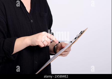 Primo piano di una giovane donna bionda con una camicia nera che punta su una clipboard, sfondo grigio studio Foto Stock