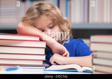 Scolaro stanco e annoiato. Bambino legge libri in biblioteca. Schoolkid con un libro nella biblioteca scolastica. Letteratura per bambini per la lettura. Imparare dai libri Foto Stock