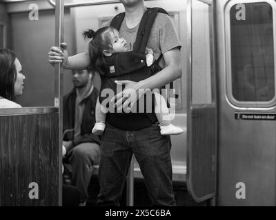 Un uomo porta una ragazza in un front pack sulla metropolitana di New York City, USA. Foto Stock