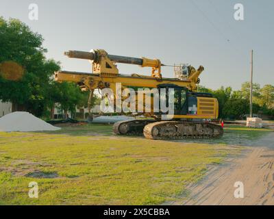 Ampia visuale di un grande CARRO DI PERFORAZIONE A ROTAZIONE giallo in erba e sporcizia con un mucchio di piccole pietre bianche sulle sezioni sinistra e dei pali di servizio in acciaio. Foto Stock