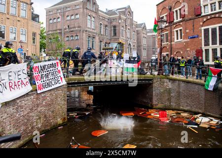 Amsterdam, Paesi Bassi. 8 maggio 2024. La polizia utilizza attrezzature per il movimento terra e getta barricate nei canali per liberare un ponte e porre fine all'occupazione studentesca pro-Palestina presso l'Università di Amsterdam. La polizia smantellò una protesta e un'occupazione studentesca pro-Palestina presso l'Università di Amsterdam, impiegando mangoni, scudi e attrezzature per il movimento terra. Il confronto è seguito quando i manifestanti si sono radunati per la solidarietà palestinese tra le tensioni, le forze dell'ordine sono intervenute per disperdere la folla, con conseguenti scontri e arresti. Credito: SOPA Images Limited/Alamy Live News Foto Stock