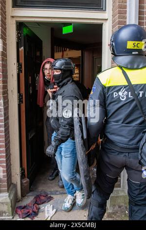 Un membro della squadra di arresto conduce uno studente arrestato fuori da un edificio amministrativo mentre la polizia ha infranto le barricate per porre fine a un'occupazione studentesca pro-Palestina presso l'Università di Amsterdam. La polizia smantellò una protesta e un'occupazione studentesca pro-Palestina presso l'Università di Amsterdam, impiegando mangoni, scudi e attrezzature per il movimento terra. Il confronto è seguito quando i manifestanti si sono radunati per la solidarietà palestinese tra le tensioni, le forze dell'ordine sono intervenute per disperdere la folla, con conseguenti scontri e arresti. Foto Stock