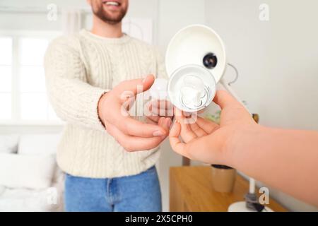 Giovane uomo che prende la lampadina per la lampada da scrivania da donna a casa, primo piano Foto Stock