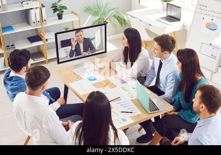 Persone d'affari che hanno una videoconferenza online nella sala riunioni con un collega uomo seduto in ufficio Foto Stock