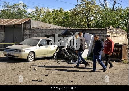 Non esclusiva: ZAPORIZHZHIA, UCRAINA - 8 MAGGIO 2024 - gli uomini passano davanti alle auto danneggiate in una cooperativa di garage dopo il massiccio missile russo An Foto Stock