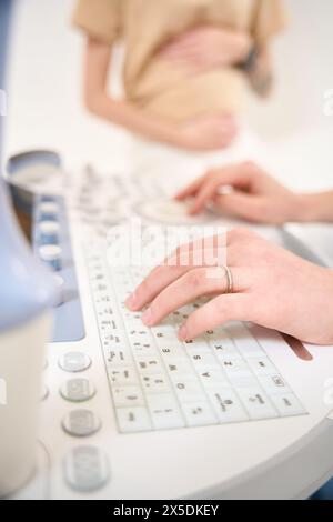 Primo piano delle mani ginecologiche utilizzando una macchina a ultrasuoni vicino a una donna sfocata Foto Stock