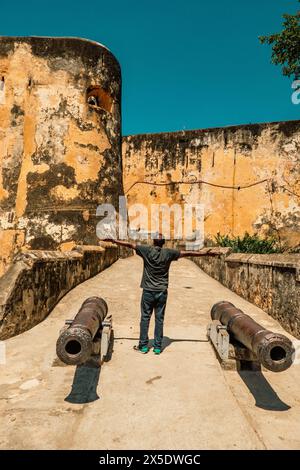 Vista posteriore di un uomo in piedi tra due cannoni all'ingresso di Fort Jesus a Mombasa Foto Stock