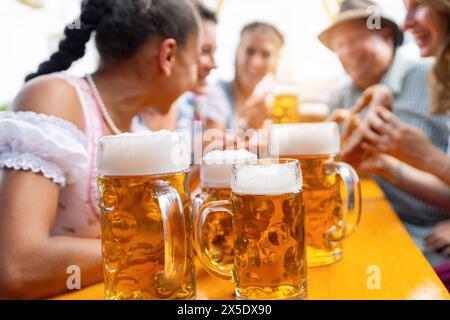 Tazze da birra su un tavolo in una tenda con amici vivaci che si gustano birre e cibo all'oktoberfest o al dult Foto Stock