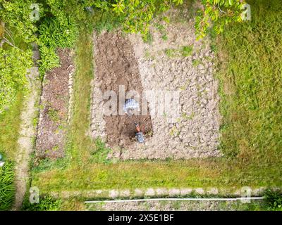 Il giovane agricoltore coltiva il campo con la macchina. Vista dall'alto di un piccolo campo con drone aereo in un giardino vecchio stile. Concetto di agricoltura domestica Foto Stock