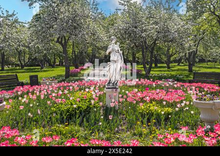 Statua in marmo dell'antica dea Diana in primavera nel parco con alberi e fiori in fiore. giornata di sole. Foto Stock