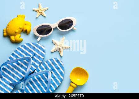 Vista dall'alto di infradito, occhiali da sole, stelle marine e giocattoli da spiaggia con spazio per copiare il testo su sfondo blu. Concetto di vacanza estiva Foto Stock