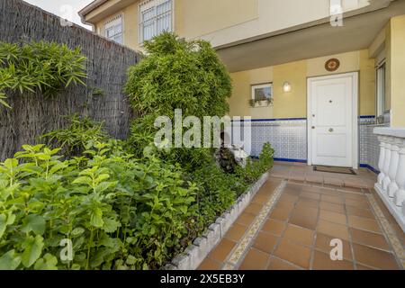 Facciata di una casa semi-indipendente con pavimenti in terracotta con balaustra di cemento bianco, area vaso di fiori con molte piante e porta di accesso bianca Foto Stock