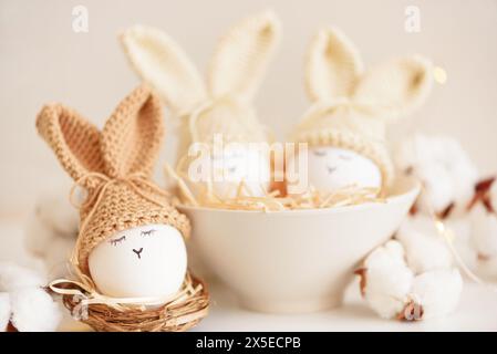 Uova di Pasqua in cappelli a maglia con orecchie di coniglio nel nido. Concetto di festa di Pasqua Foto Stock