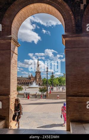 Una donna bionda sale i gradini con Plaza de Espana a Siviglia, Spagna, incorniciata da un arco sullo sfondo Foto Stock