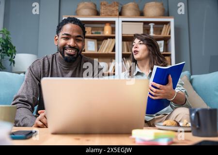 Coppia hipster positiva che si diverte lavorando insieme da remoto a casa utilizzando la tecnologia moderna, allegri giovani uomini d'affari e donne che ridono. Foto Stock