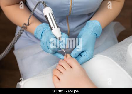 L'esperto di pedicure esegue una pedicure hardware su una donna, impiegando un trapano per unghie Foto Stock