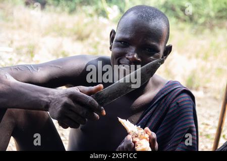 I membri della tribù Mursi in Etiopia, nella valle dell'Omo, si sono riuniti intorno al fuoco, mangiando carne di ossa animali, vita primitiva in un luogo remoto in Africa Foto Stock