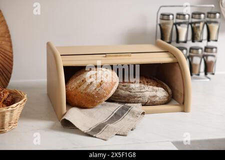 Cestino di pane in legno con pane appena sfornato su un tavolo in marmo bianco in cucina Foto Stock