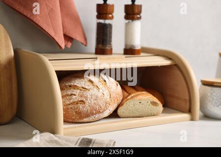 Cestino di pane in legno con pane appena sfornato su un tavolo in marmo bianco in cucina Foto Stock