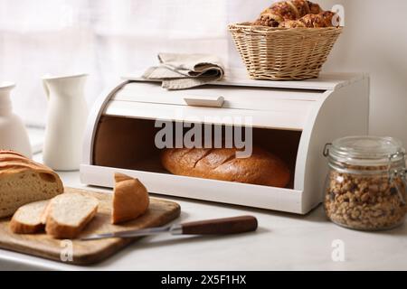 Cestino di pane in legno con pane appena sfornato su un tavolo in marmo bianco in cucina Foto Stock