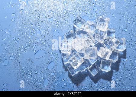 Pile di cubetti di ghiaccio e gocce d'acqua su sfondo blu, vista dall'alto. Spazio per il testo Foto Stock