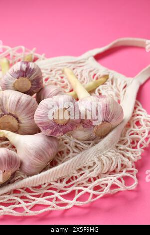 Borsa a cordoncino con teste d'aglio su sfondo rosa brillante, primo piano Foto Stock