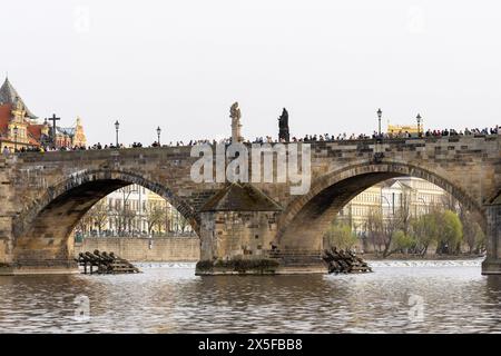 Praga, repubblica ceca - 3 marzo 2024: Turisti che camminano sul ponte Carlo visto sotto dal fiume Moldava Foto Stock