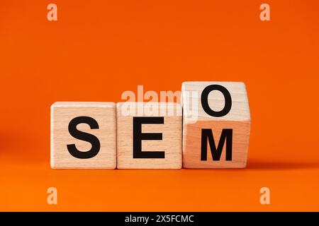 La parola SEO che cambia in SEM, scritta in cubi di legno su uno splendido sfondo arancione, Concept for Search Engine Optimization e Search Engine Matketi Foto Stock