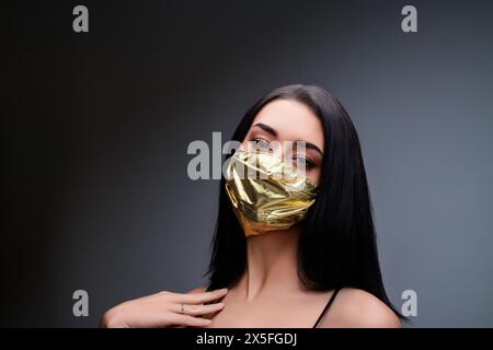 aumento di prezzo di maschere facciali e scarsità in COVID-19 volte concetto come una bella giovane donna che indossa una maschera facciale in oro perché può permetterselo Foto Stock