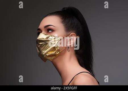 aumento di prezzo di maschere facciali e scarsità in COVID-19 volte concetto come una bella giovane donna che indossa una maschera facciale in oro perché può permetterselo Foto Stock