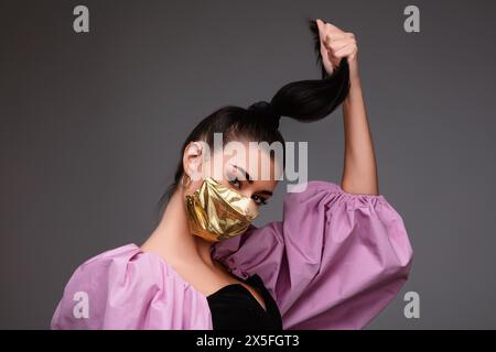 aumento di prezzo di maschere facciali e scarsità in COVID-19 volte concetto come una bella giovane donna che indossa una maschera facciale in oro perché può permetterselo Foto Stock