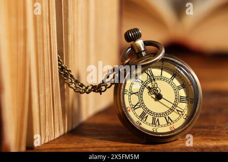 Orologio tascabile con catena e libro su tavolo in legno, primo piano Foto Stock