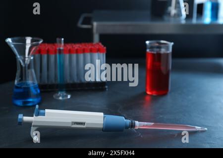 Analisi di laboratorio. Micropipetta e vetreria diversa su un tavolo nero Foto Stock