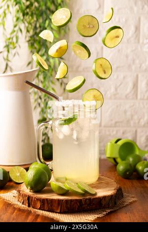 Fette di limoni freschi che cadono sul bicchiere con limonata fatta in casa, bicchiere con paglia metallica e decorato con fette di limone. Foto Stock