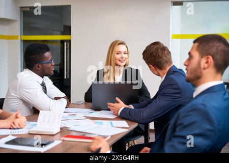 Il team multirazziale si occupa di riunioni aziendali, mentre i rappresentanti aziendali africani e caucasici discutono i progetti con il team leader femminile in un ufficio moderno, presentando i progetti Foto Stock