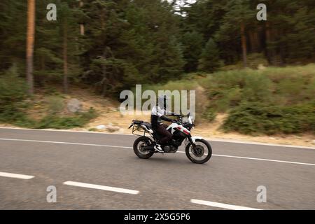 motociclista vestito di nero in moto su strada con casco inserito, che guida ad alta velocità Foto Stock