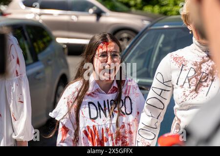 Una donna Ucraina che indossa un vestito con la parola DNIPRO scritta su di esso e dipinta con urla di sangue mentre l'ambasciatore russo posa fiori il giorno della vittoria sui nazisti al cimitero dei soldati sovietici attivisti ucraini protestano di fronte al cimitero dei soldati sovietici il giorno della vittoria sul nazismo. Donne ucraine vestite con abiti bianchi con città ucraine che sono state distrutte durante la guerra con la Russia scritto su di loro, questi abiti sono stati spalmati di sangue sintetico. Questo evento si è svolto il 9 maggio a Varsavia. Foto Stock