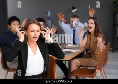 Giovane donna d'affari con tappi per le orecchie che soffre di colleghi rumorosi in ufficio Foto Stock