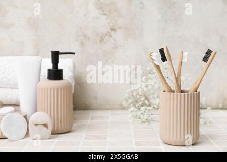 Set di articoli da bagno con spazzolini da denti in bambù su un tavolo con piastrelle leggere Foto Stock