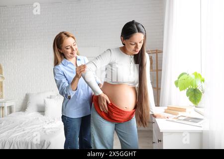 Doula matura massaggia una donna incinta con sciarpa in camera da letto Foto Stock