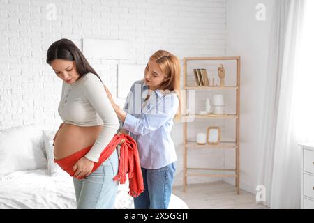 Doula matura massaggia una donna incinta con sciarpa in camera da letto Foto Stock