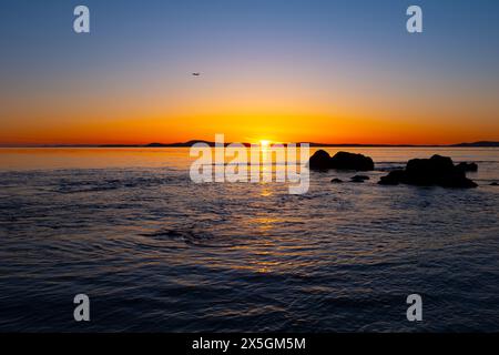 WA24843-00....WASHINGTON - tramonto sullo stretto di Rosario e sul Mare di Salish con un aereo nel cielo. Vista da West Point Beach su Whidbey Island, Foto Stock