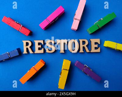 Vista dall'alto clip in legno e parola in legno con testo RIPRISTINATO su sfondo blu. Foto Stock