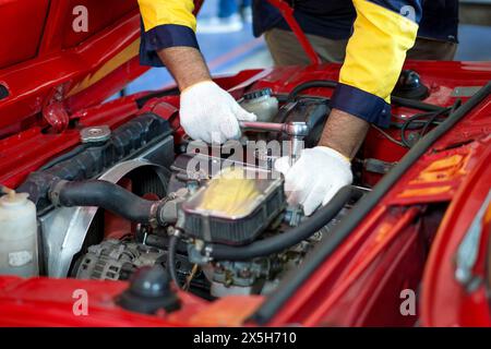 Il meccanico di primo piano indossa l'uniforme da lavoro, lavora su un'auto in un'officina automobilistica o in un'officina. Sembra concentrato e impegnato nella diagnosi o nella riparazione del ve Foto Stock