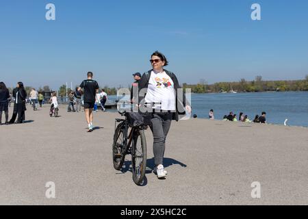 Belgrado, Serbia, 23 marzo 2024: Una donna spinge piacevolmente una bicicletta lungo il molo di Zemun. Foto Stock