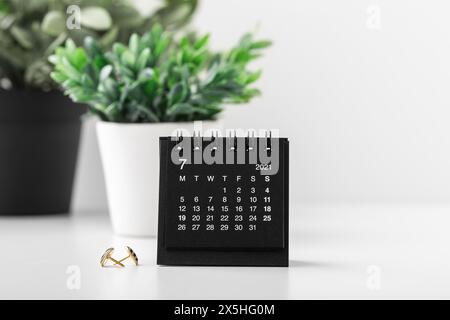Calendario nero con pianta in pentole sulla scrivania bianca, copia spazio Foto Stock