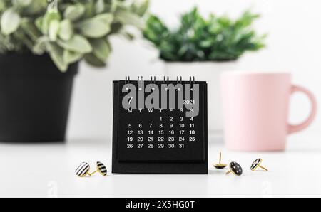 Calendario nero con spille e piante verdi sul tavolo bianco Foto Stock