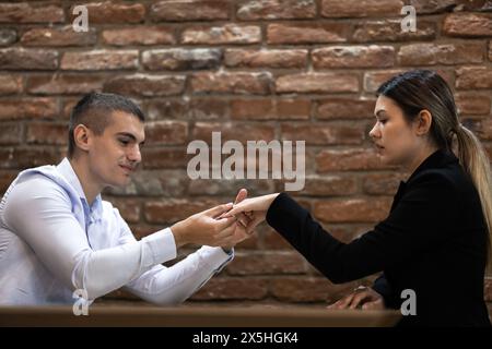 Un giovane uomo e una donna si stanno impegnando in uno scambio professionale di biglietti da visita sullo sfondo di un muro di mattoni in un accogliente caffè. Foto Stock