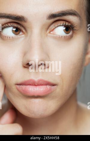 Questa immagine ravvicinata presenta una giovane donna con accattivanti occhi di nocciola e un trucco minimale, che mette in risalto la bellezza naturale e le sottili espressioni facciali. Foto Stock